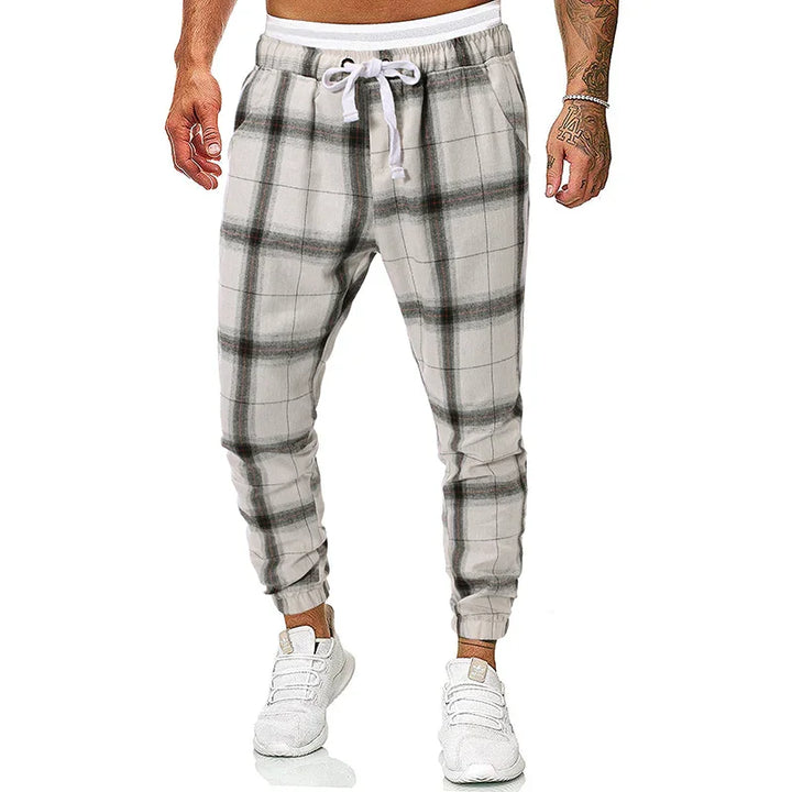Men's gray and white plaid jogger pants with white drawstring and elastic cuffs, worn with white sneakers