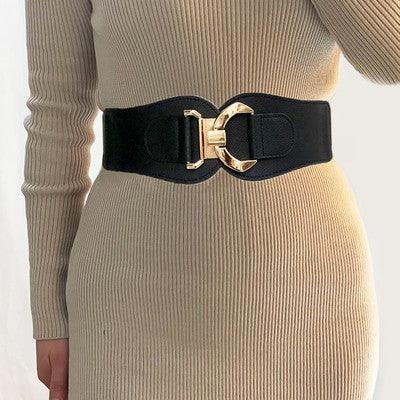 Woman wearing a beige ribbed knit dress with a wide black belt featuring a gold buckle