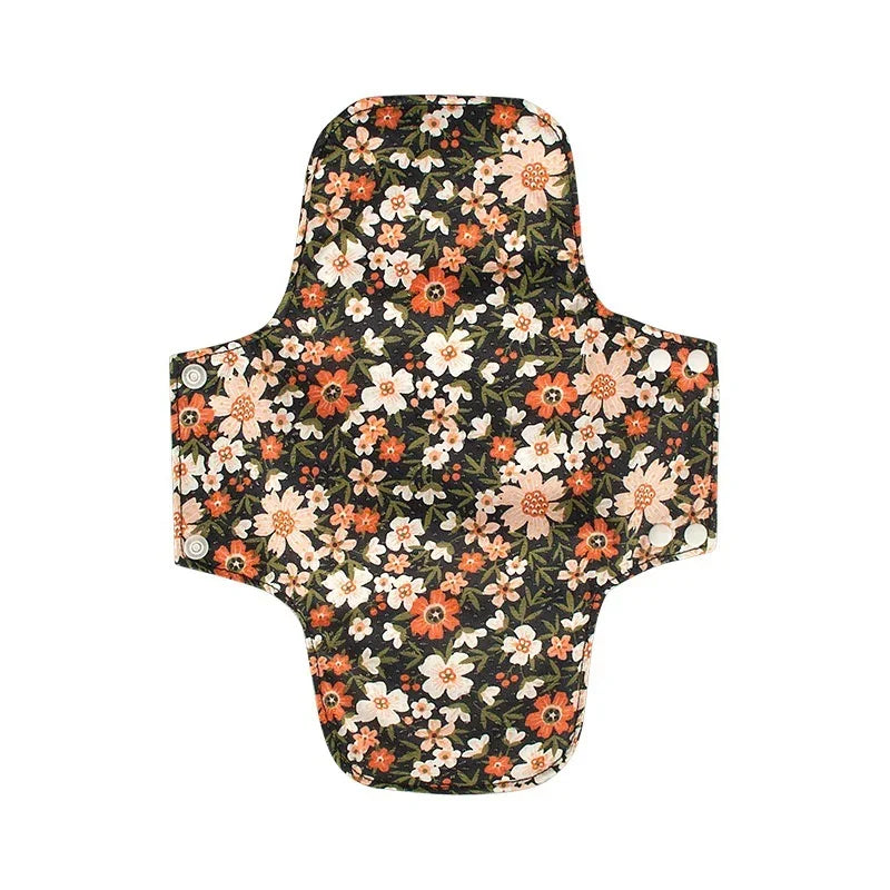 Reusable fabric menstrual pad with floral pattern in orange, white, and green on black background