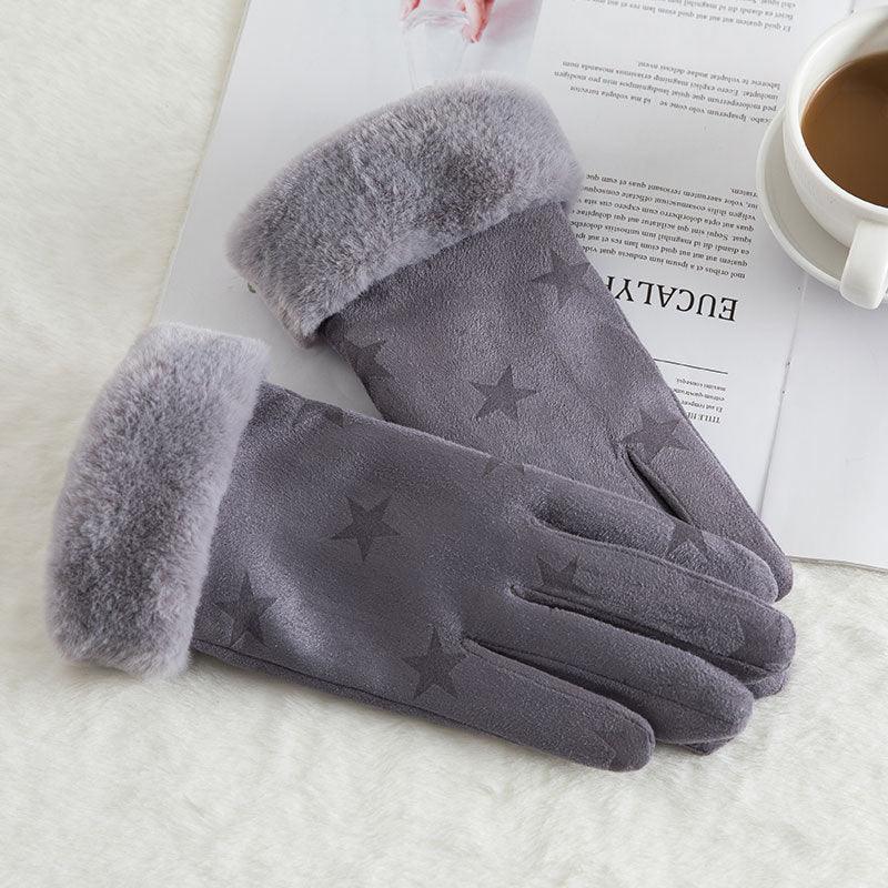 Pair of gray winter gloves with star patterns and fluffy cuffs on a white surface next to a cup of coffee