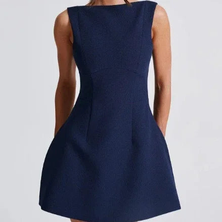 Woman wearing a sleeveless navy blue A-line dress with pockets on light gray background