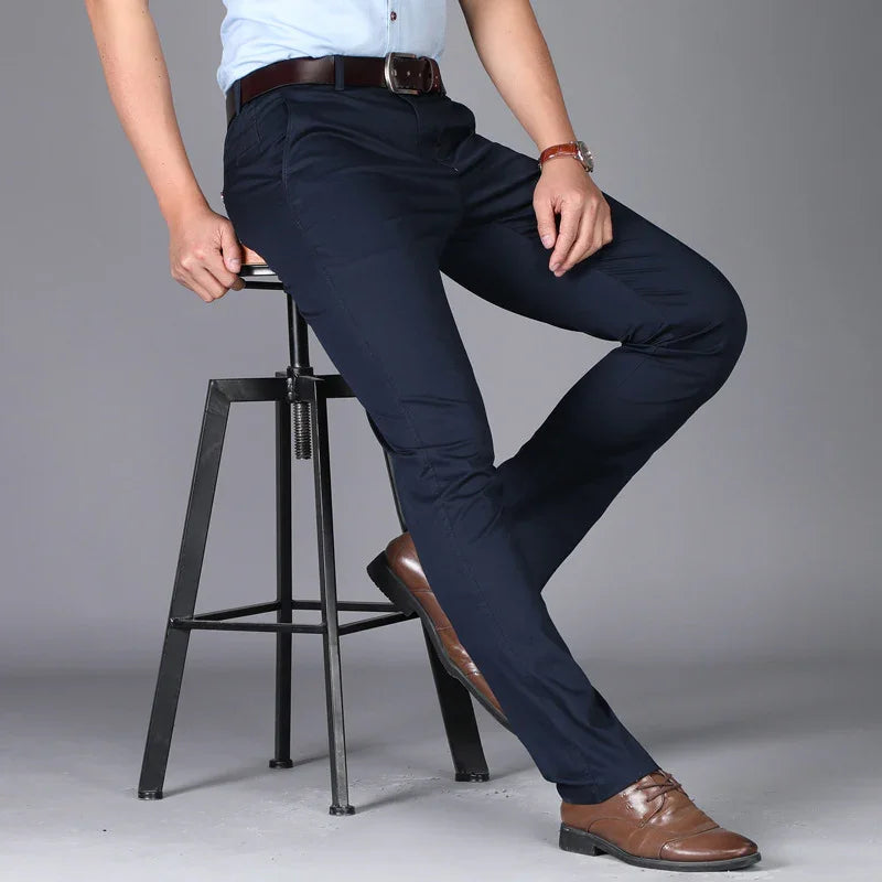 Man wearing slim fit navy blue trousers with brown leather belt and shoes, sitting on black metal stool