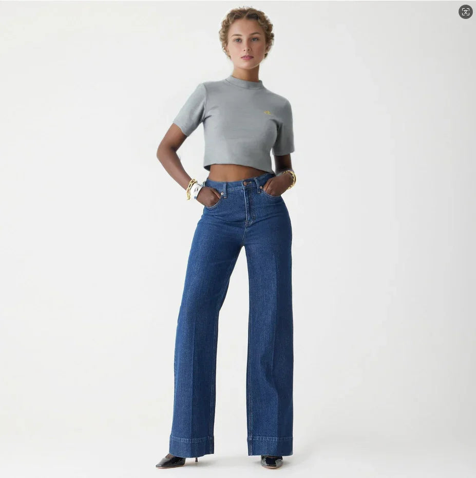 Woman wearing gray cropped t-shirt and high-waisted blue wide-leg jeans against white background