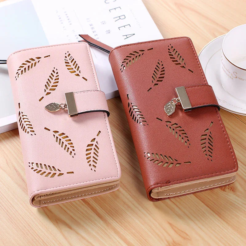Pink and brown leather wallets with leaf cutout design and metal leaf charm on wooden table