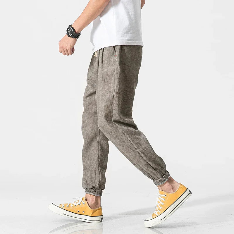 Man wearing gray jogger pants, white t-shirt, yellow sneakers, and black watch walking on white background