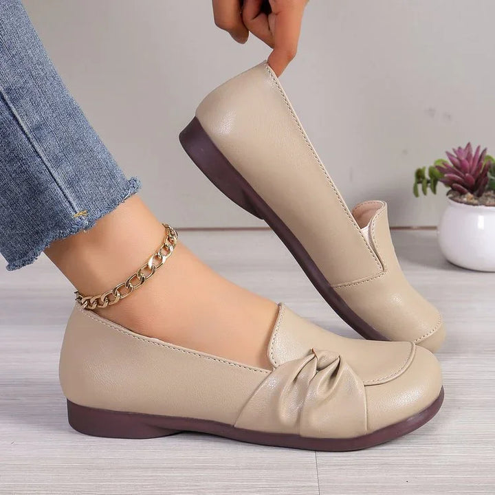 Beige leather flat shoes with ruched detail worn with blue jeans and a gold ankle chain