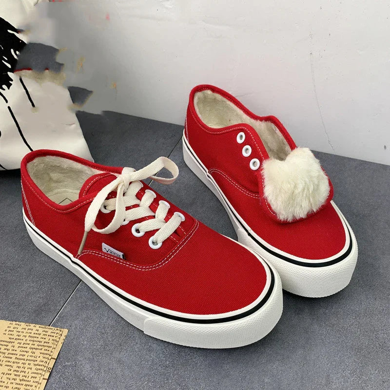 Pair of red canvas sneakers with white rubber soles and fur lining, one with laces tied, on gray surface