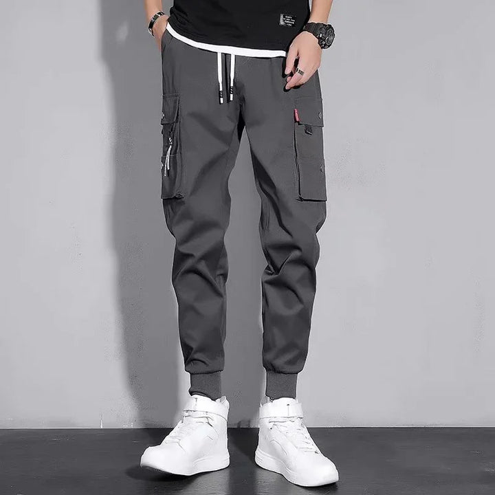 Men's dark gray cargo jogger pants with multiple pockets worn with white high-top sneakers