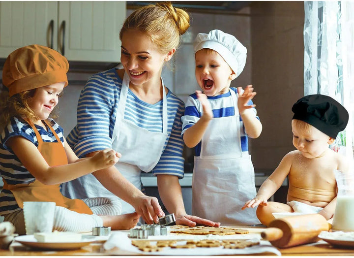 Smiling mother and three children baking cookies together, wearing aprons and chef hats in kitchen
