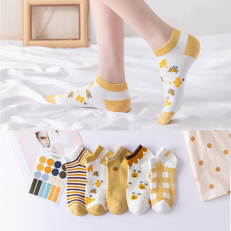 White ankle socks with yellow bee and honeycomb designs, displayed on feet and in a set of five pairs