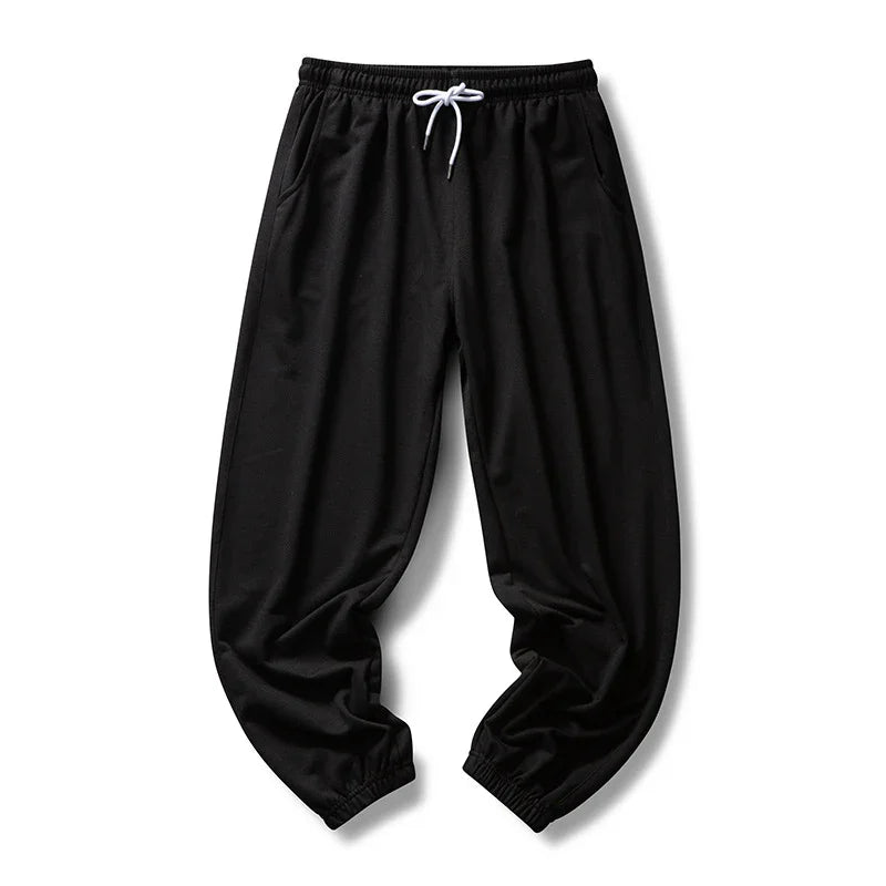 Black casual jogger pants with elastic cuffs and white drawstring on white background