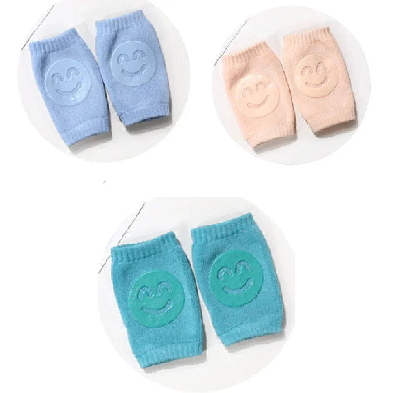 Three pairs of soft baby knee pads in blue, peach, and teal with smiley face grips