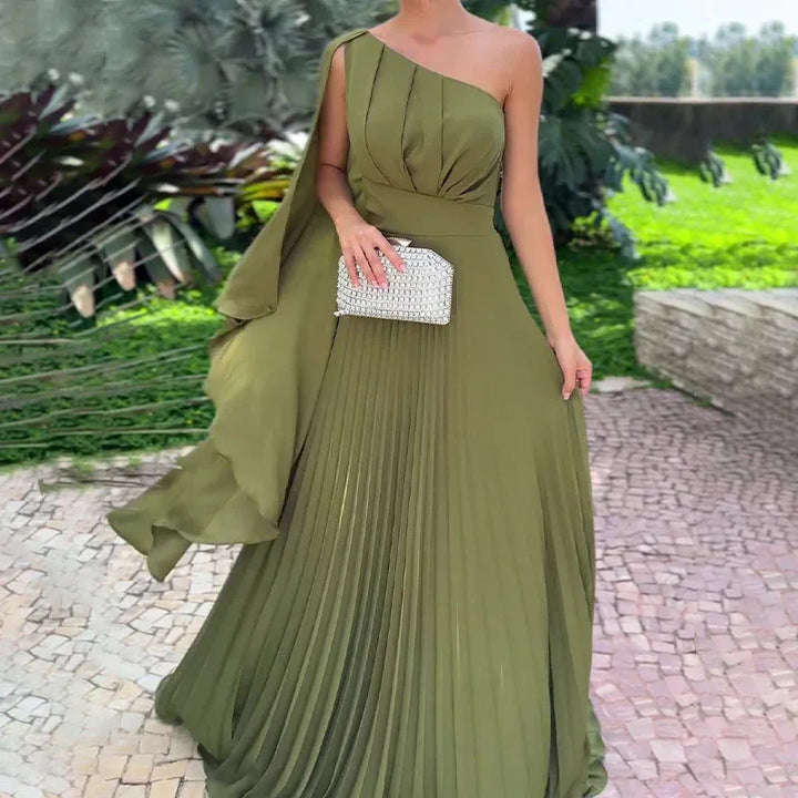 Woman wearing an elegant olive green one-shoulder pleated dress holding a silver clutch outdoors