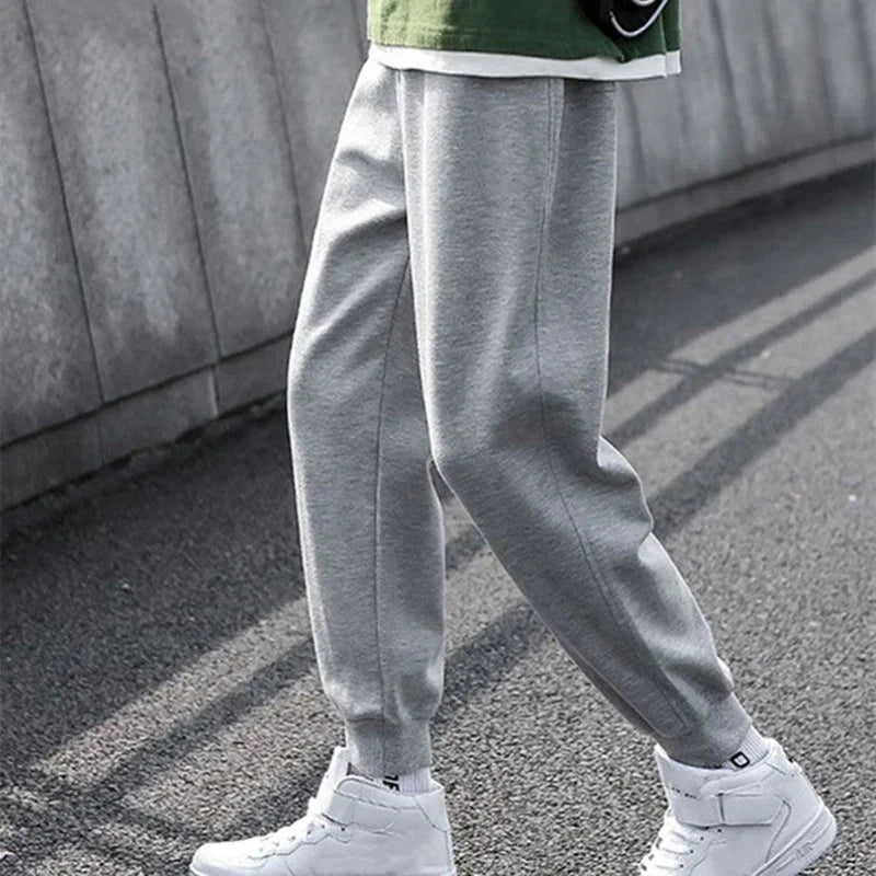 Person wearing gray jogger pants and white sneakers walking on asphalt near a concrete wall
