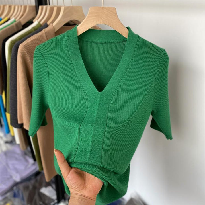 Hand holding green knitted V-neck short sleeve sweater on wooden hanger with other sweaters in background