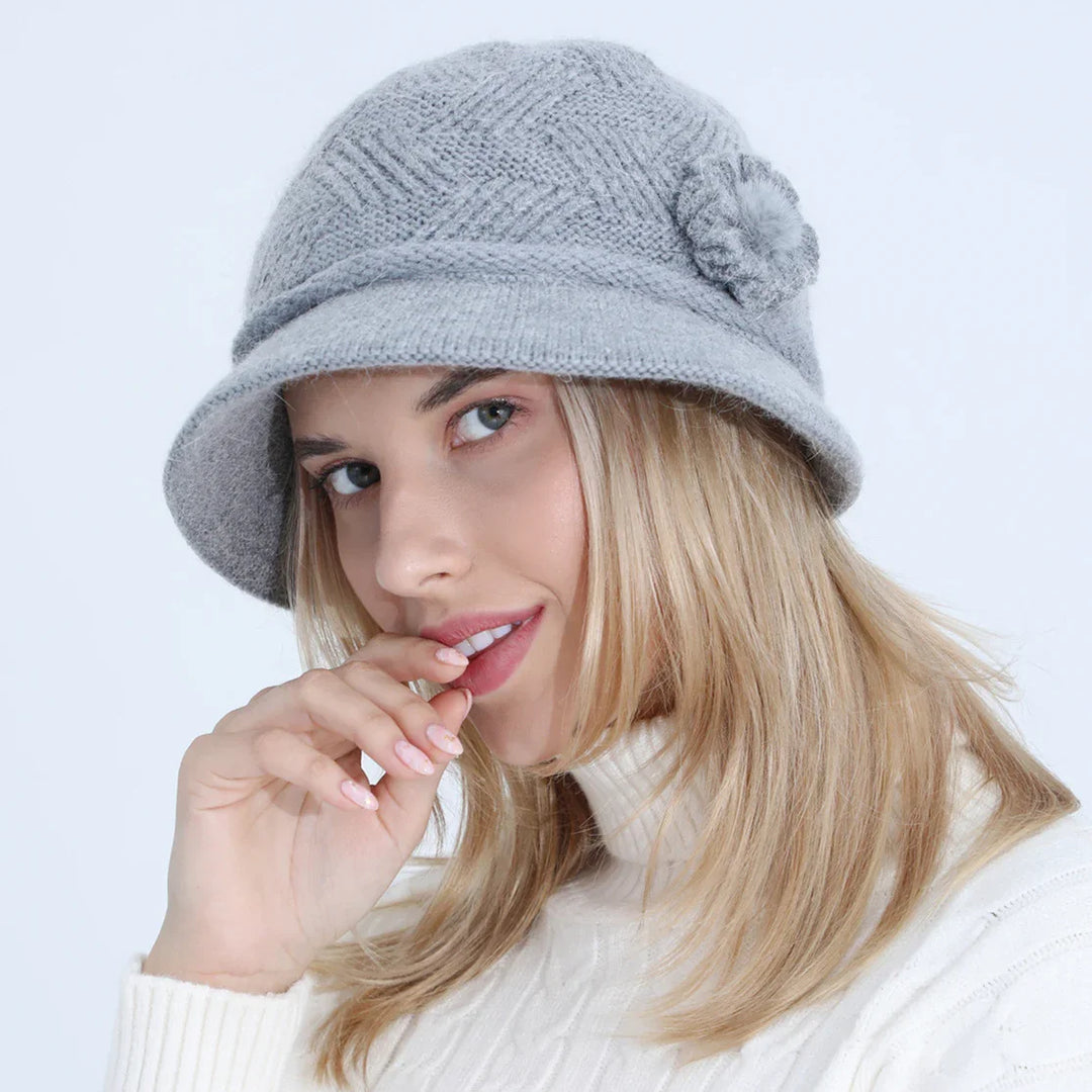 Blonde woman wearing a gray knitted cloche hat with a flower detail and white turtleneck sweater