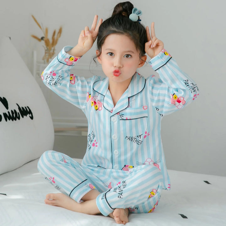 Girl in blue and white striped Pink Panther pajamas making a playful pose sitting on a bed