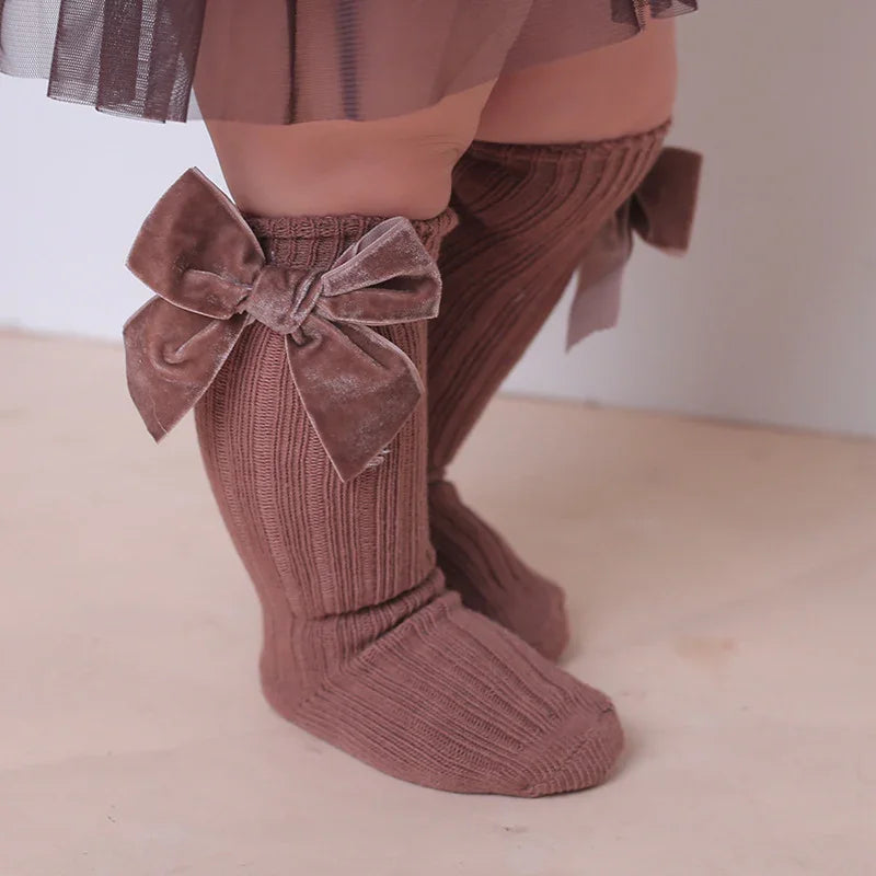 Baby legs wearing brown ribbed knee-high socks with large velvet bows and a brown tulle skirt