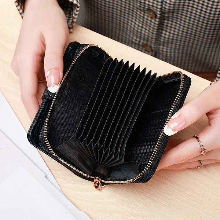 Hands holding open black accordion-style zippered card wallet with gold zipper on wooden table