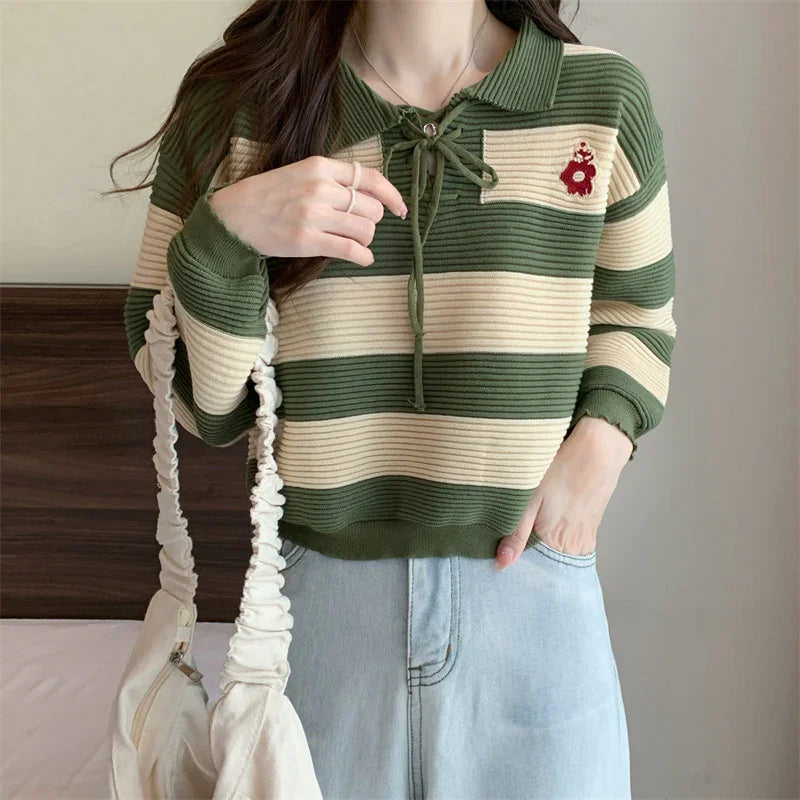 Woman wearing green and cream striped knit sweater with collar and embroidered bear detail, light denim jeans, and carrying white ruched bag