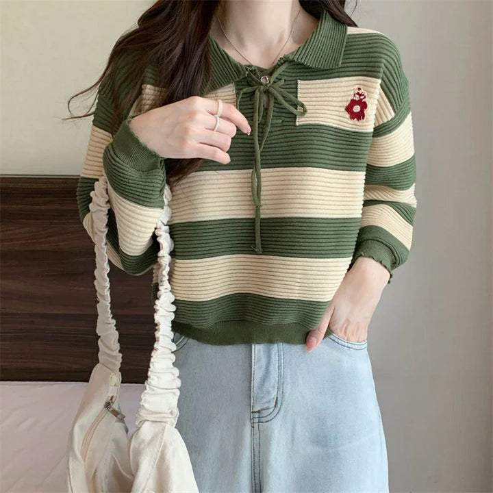 Woman wearing green and cream striped knit sweater with collar and embroidered bear detail, light denim jeans, and carrying white ruched bag