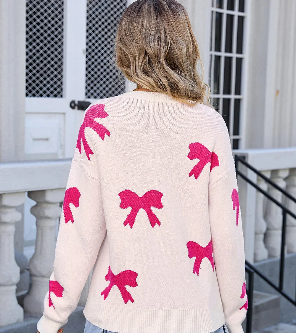 Woman wearing cream sweater with pink bow patterns, standing outdoors near white building steps