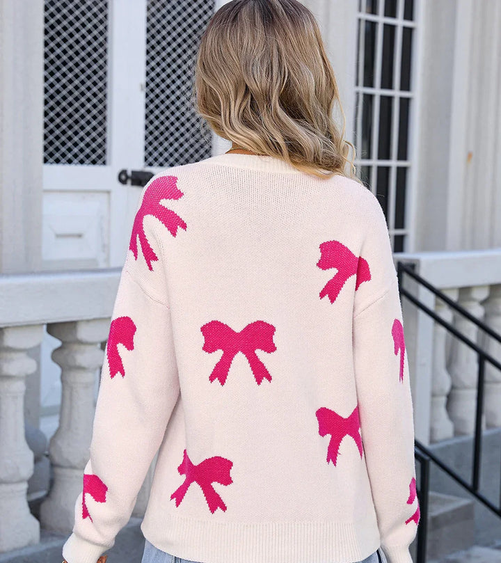 Woman wearing cream sweater with pink bow patterns, standing outdoors near white building steps