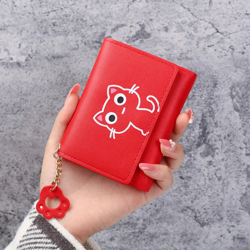 Red wallet with cute cartoon cat print and paw keychain held in hand on gray stone background