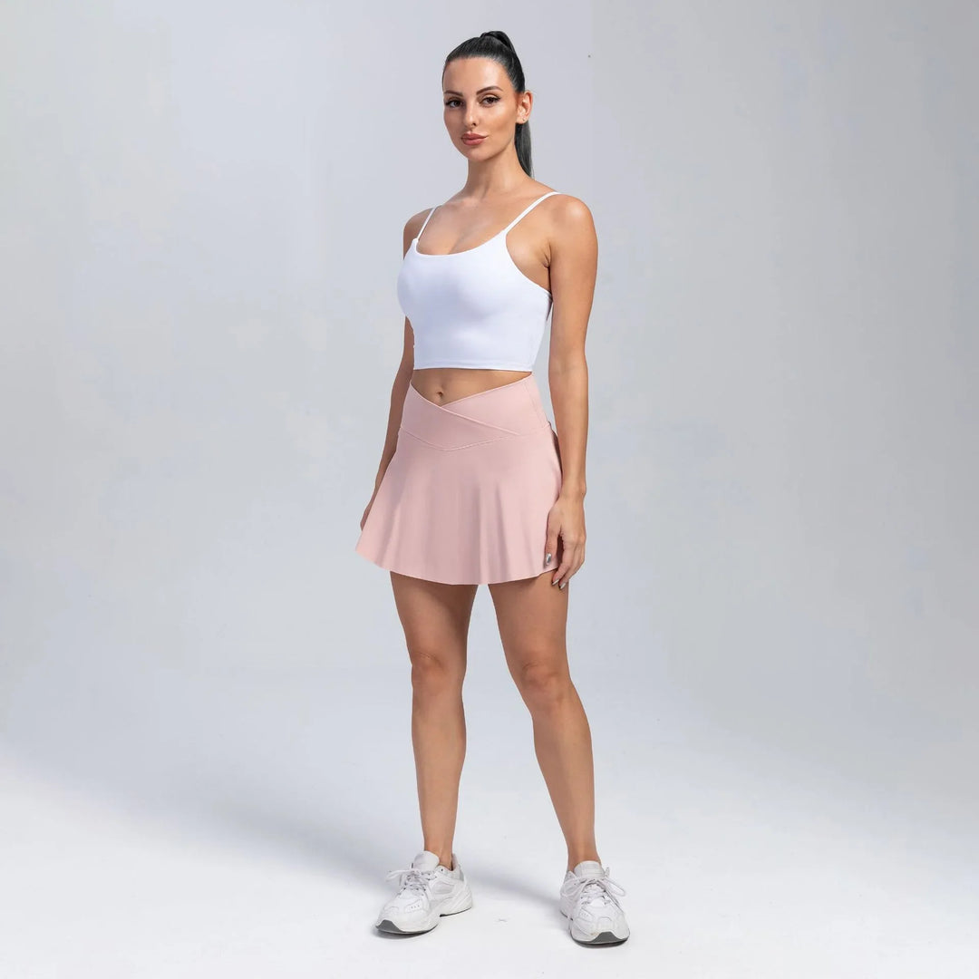 Woman in white crop top, pink athletic skirt, and white sneakers posing on plain background
