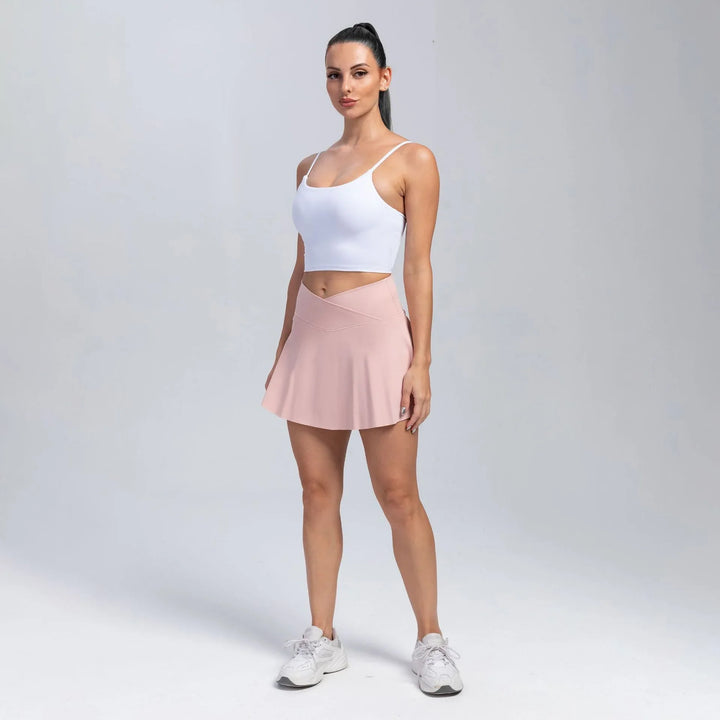 Woman in white crop top, pink athletic skirt, and white sneakers posing on plain background