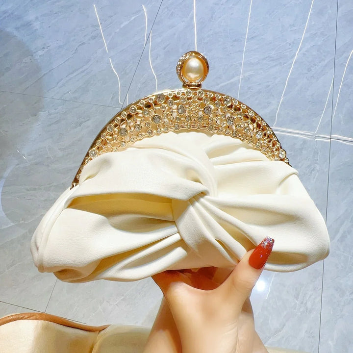 Elegant cream clutch purse with twisted fabric and gold rhinestone decorative clasp held by hand