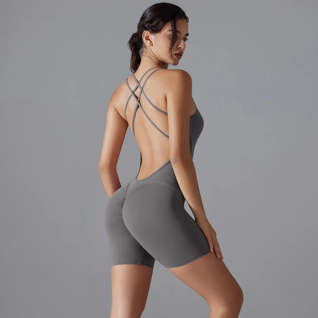 Woman wearing gray seamless open-back workout romper with crisscross straps against gray background