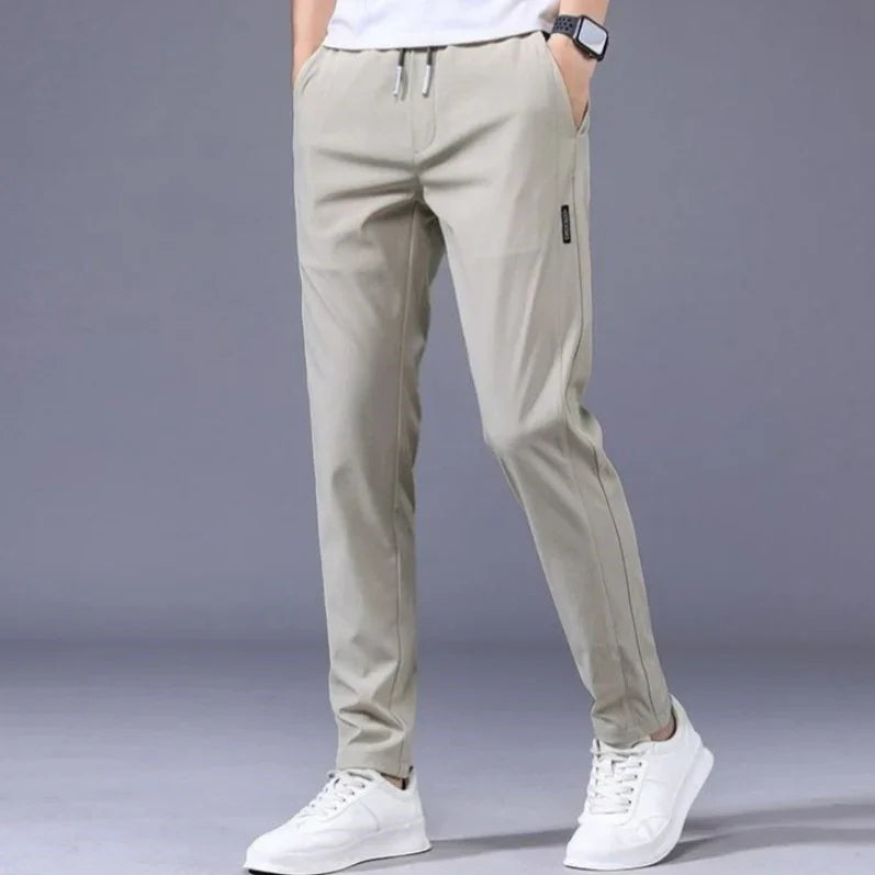 Men's casual light beige jogger pants with drawstring waist and white sneakers on gray background