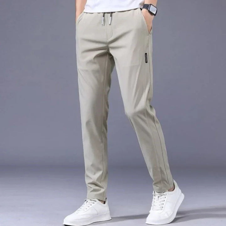 Men's casual light beige jogger pants with drawstring waist and white sneakers on gray background