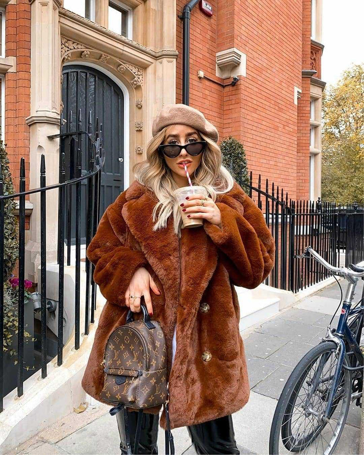 Woman in brown faux fur coat, beige beret, sunglasses, holding Louis Vuitton backpack and iced coffee on city sidewalk