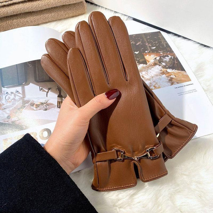Hand holding brown leather gloves with gold buckle detail on white fur background