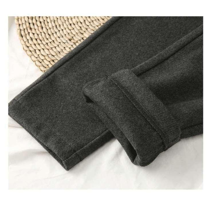 Close-up of dark gray woolen pants leg with cuff detail on white fabric and woven placemat