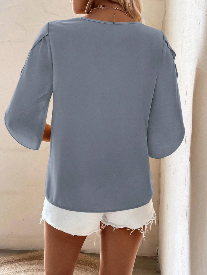 Woman wearing light blue loose top with elbow-length sleeves and white frayed shorts, back view