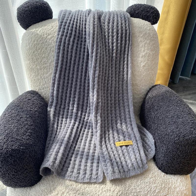 Grey knitted scarf with handmade tag draped over black and white plush armchair with round armrests