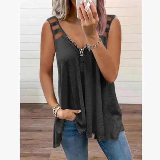 Woman wearing black sleeveless zipper top with cutout straps and blue jeans, standing on wooden floor