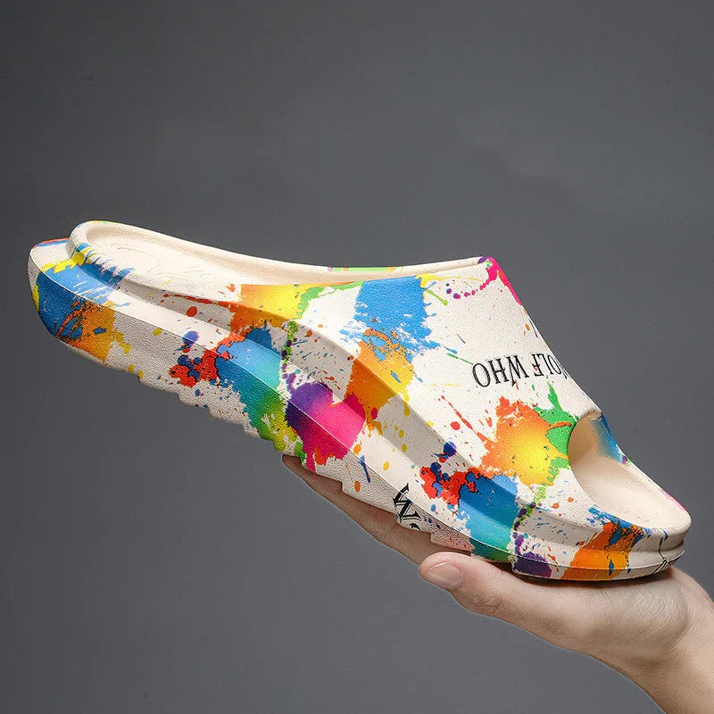 Hand holding colorful white slide sandal with vibrant paint splatter design and text