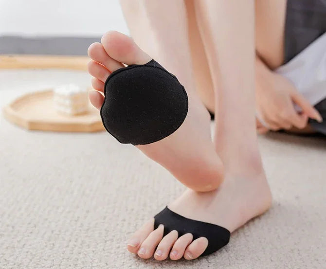Person wearing black metatarsal foot pad on bare foot, sitting on beige carpet