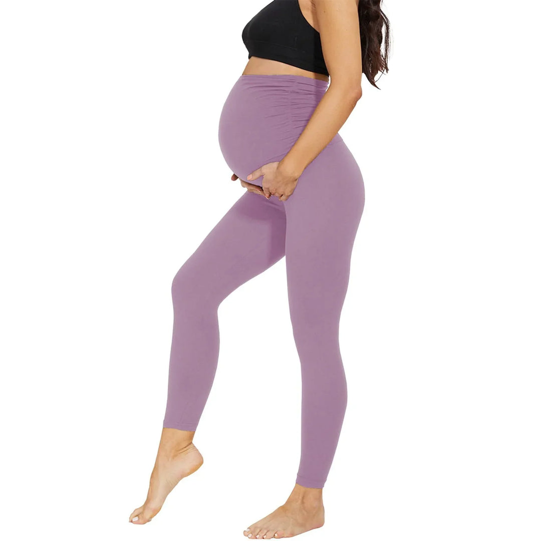 Pregnant woman wearing lavender maternity leggings and a black crop top against white background