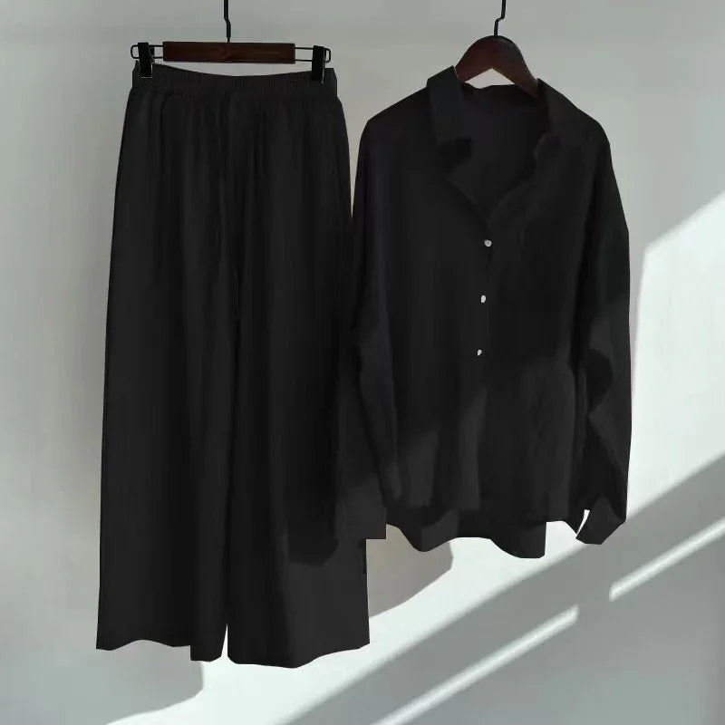 Black loose pants with elastic waist and matching black button-up shirt on hangers against white wall