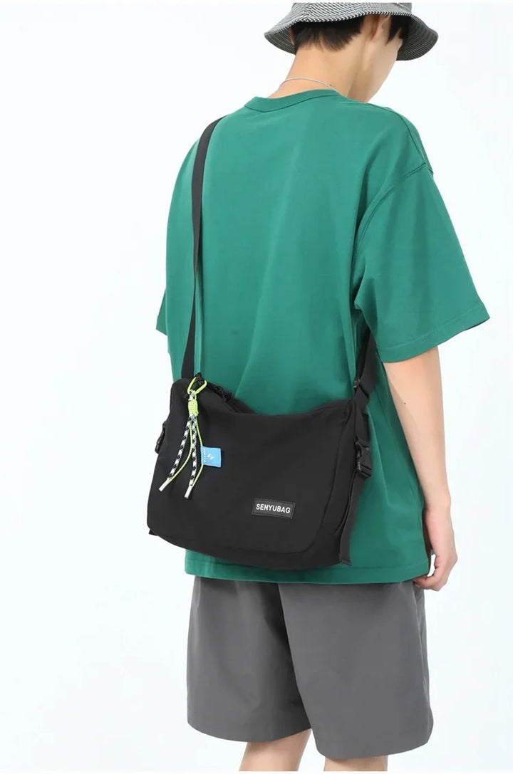 Person wearing a green t-shirt, gray shorts, and bucket hat carrying a black Senyubag shoulder bag