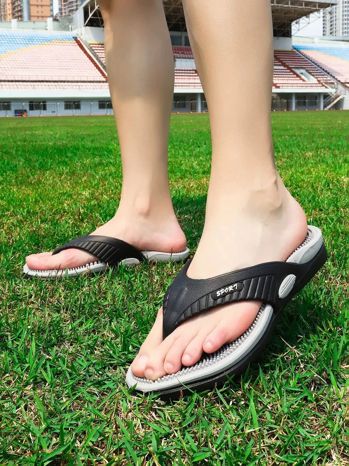 Feet wearing black and gray sport flip-flops standing on green grass at a stadium