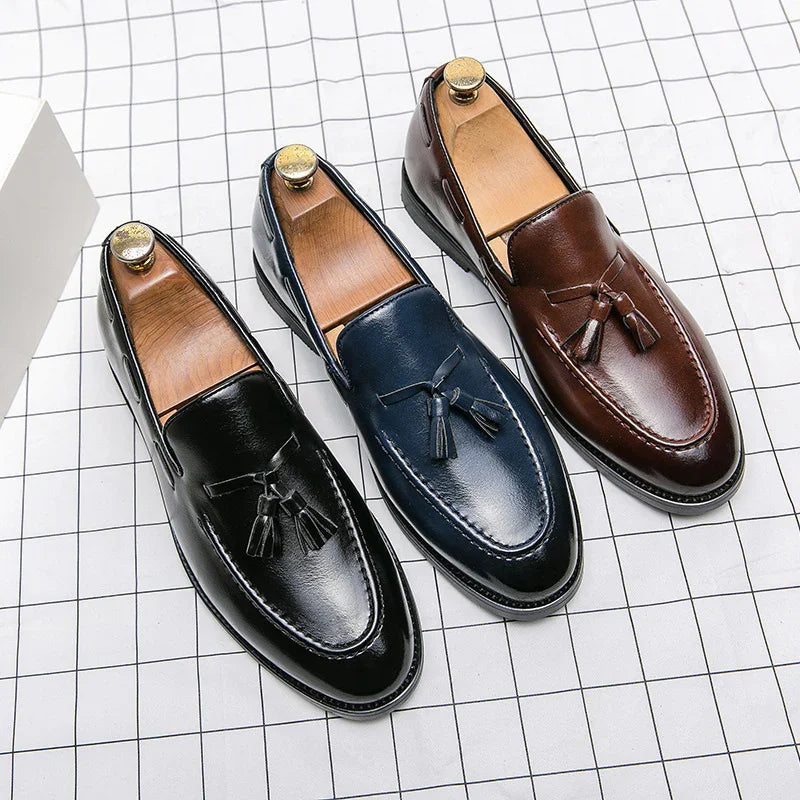 Three pairs of men's leather tassel loafers in black, navy, and brown on a white grid surface