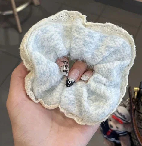 Hand holding a textured white fabric scrunchie with lace trim, showcasing manicured nails with black and white bow designs