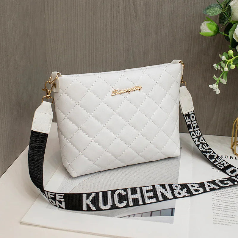 White quilted crossbody bag with gold logo and detachable black and white strap on table
