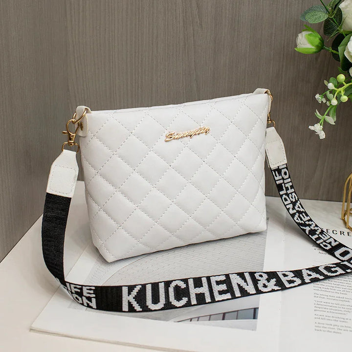 White quilted crossbody bag with gold logo and detachable black and white strap on table